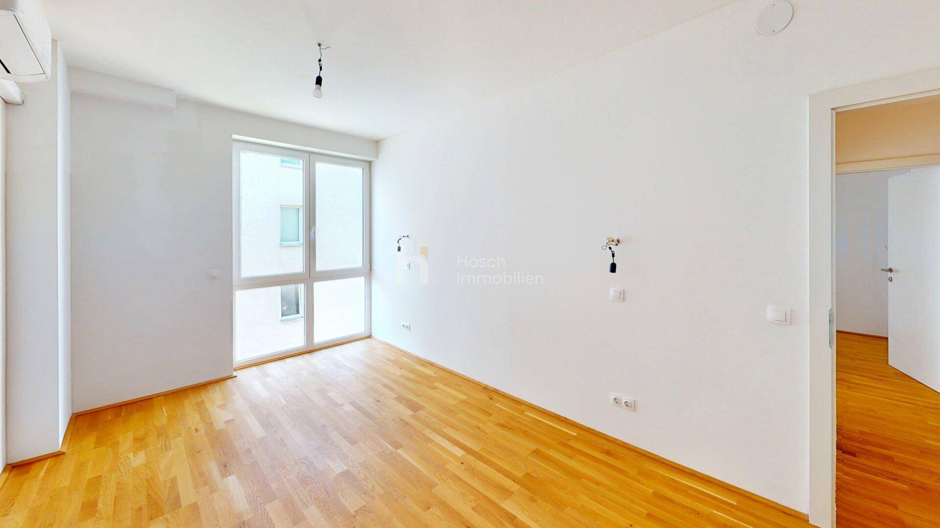 Lichtdurchflutetes Schlafzimmer mit Holzfußboden und großem Fenster.