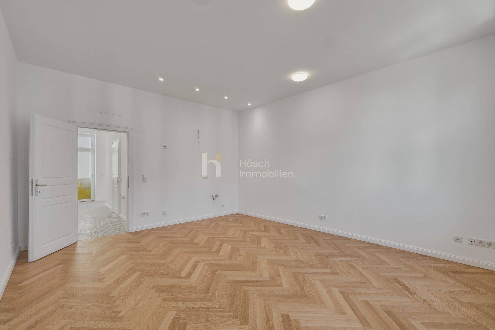 Geräumiges Zimmer mit elegantem Fischgrätparkett und weiß gestrichenen Wänden.
