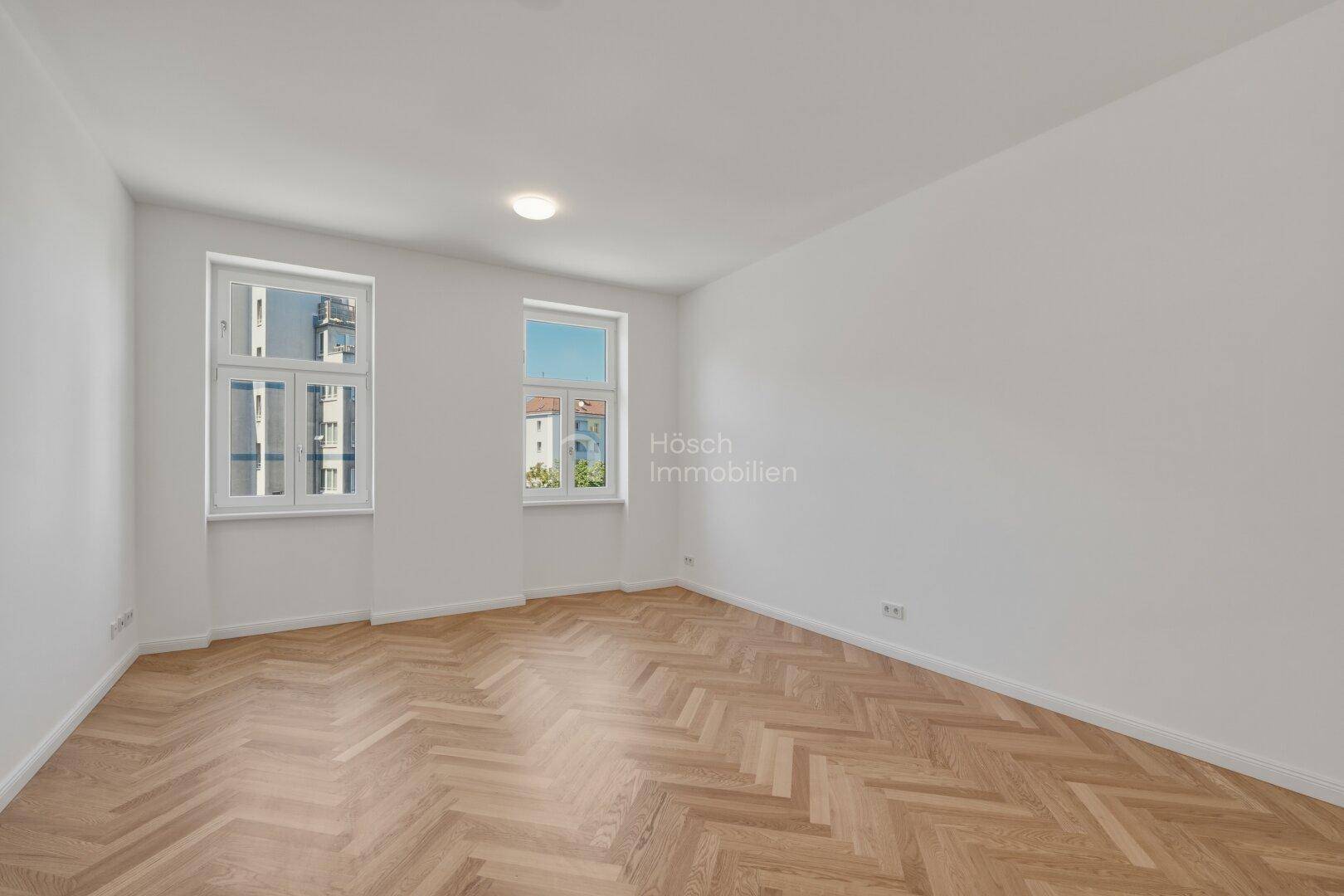 Lichtdurchflutetes Zimmer mit elegantem Fischgrätparkett und großen Fenstern.