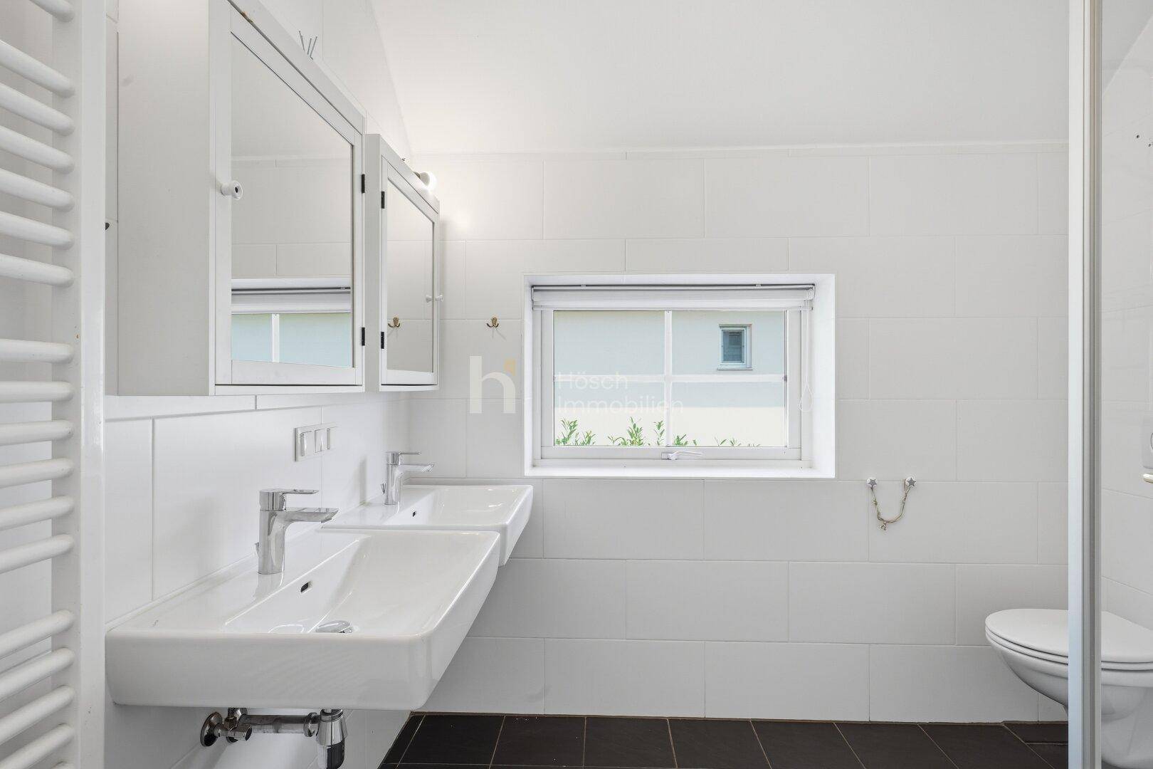 Modernes Badezimmer mit Doppelwaschbecken, Spiegelschränken und einem Fenster für Tageslicht.