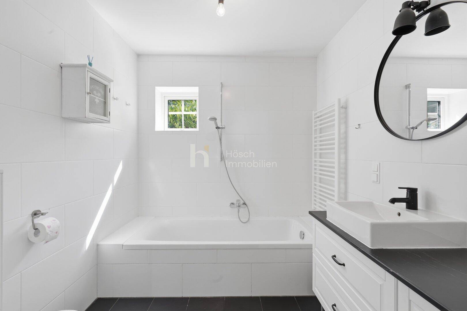 Modernes Badezimmer mit Badewanne, Einzelwaschbecken und einem runden Spiegel.