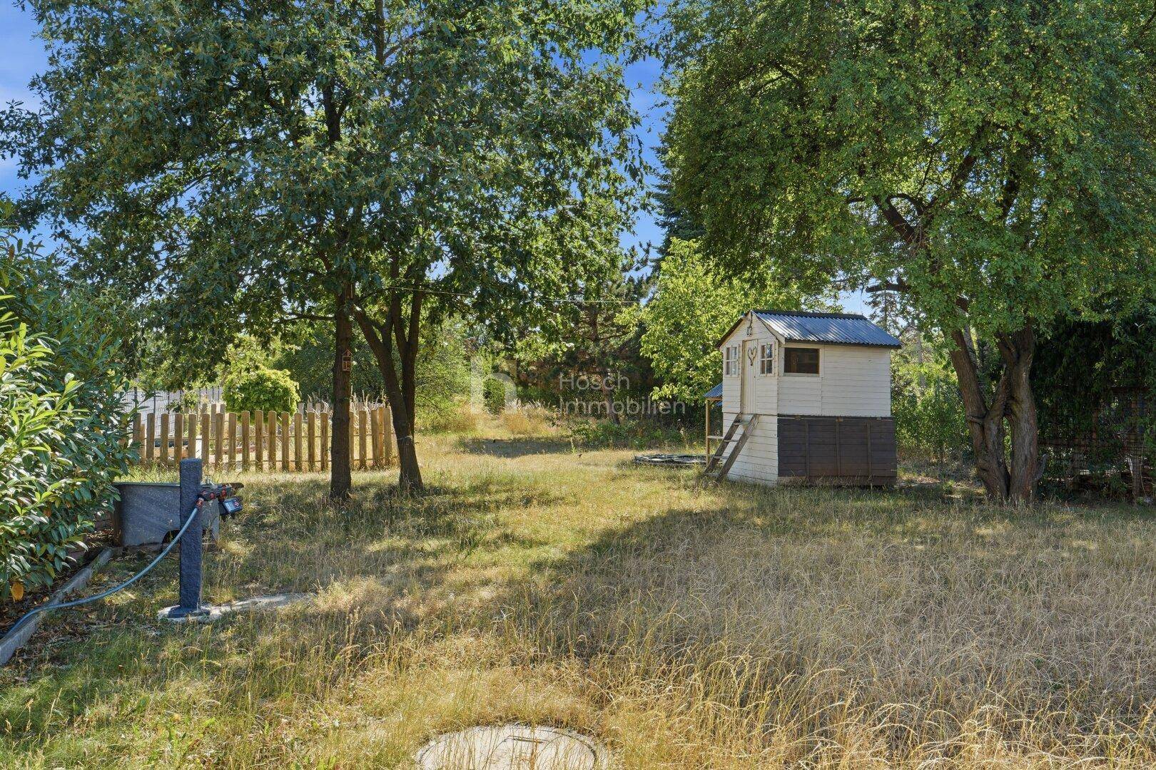 Großer, naturbelassener Gartenbereich mit Bäumen, Rasen und einem kleinen Gartenhaus.