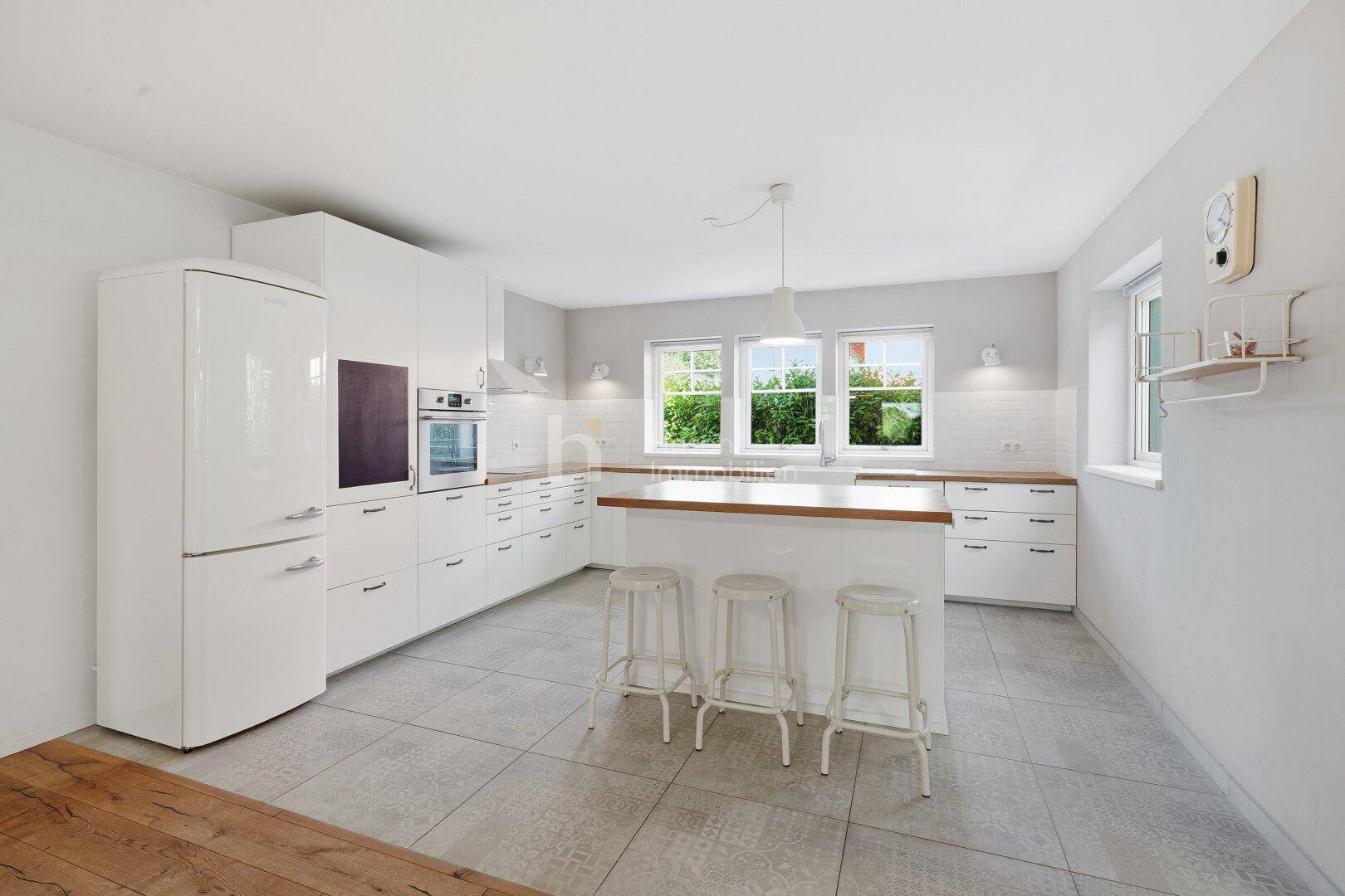Moderne Küche mit weißen Schränken, Holz-Arbeitsplatten, Kücheninsel und einem freistehenden Kühlschrank.
