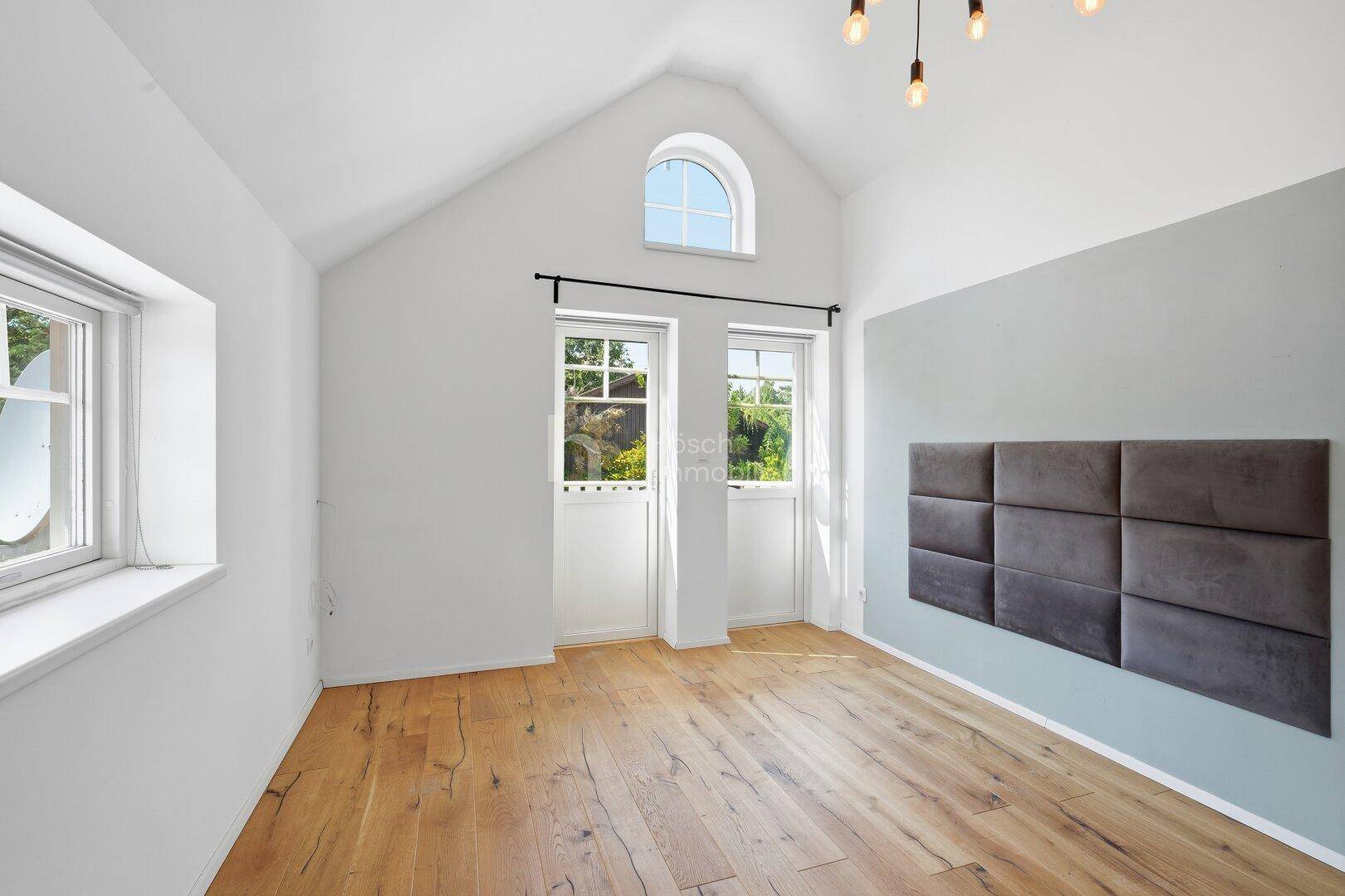 Helles Schlafzimmer mit Holzboden, Dachschräge und Zugang zu einem französischen Balkon.
