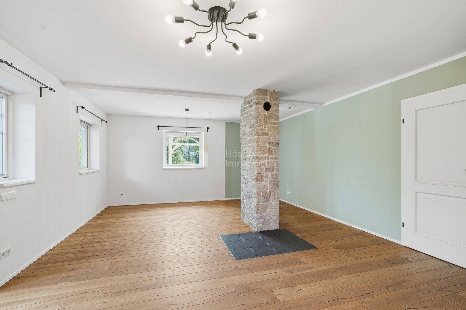 Heller Wohnbereich mit Holzboden, einer steinverkleideten Säule und einem modernen Deckenleuchter.