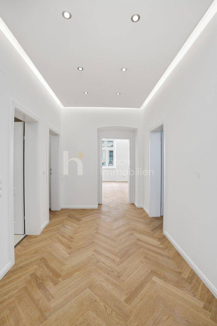 Heller Flur mit Fischgrätparkettboden, weißen Wänden und moderner Deckenbeleuchtung.
