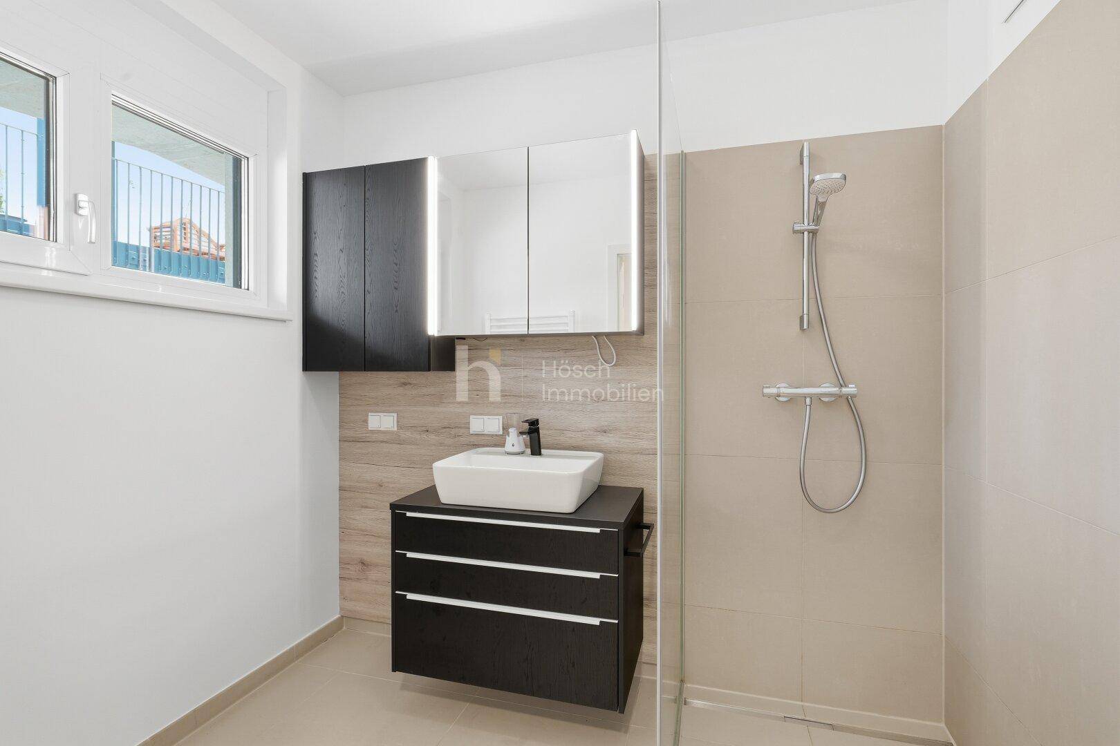 Modernes Badezimmer mit ebenerdiger Dusche, Waschtisch und Spiegelschrank, sowie einem Fenster.