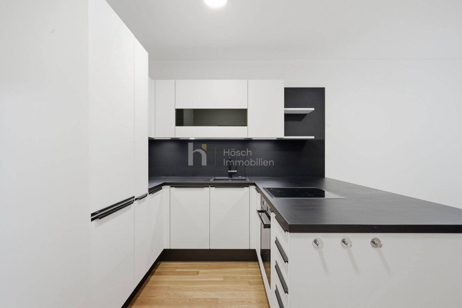 Moderne Einbauküche mit weißen Fronten, dunkler Arbeitsplatte und integrierten Geräten.