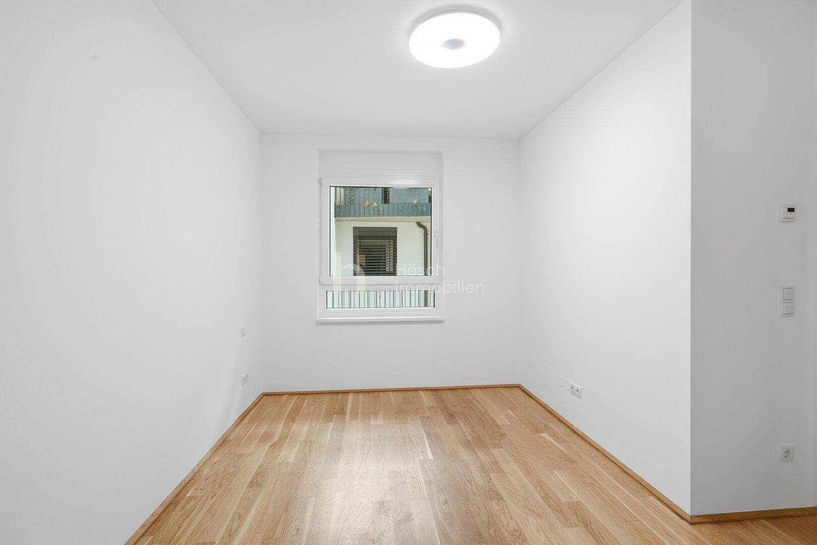 Helles Zimmer mit Holzboden und Fenster, das einen ruhigen Blick nach außen bietet.
