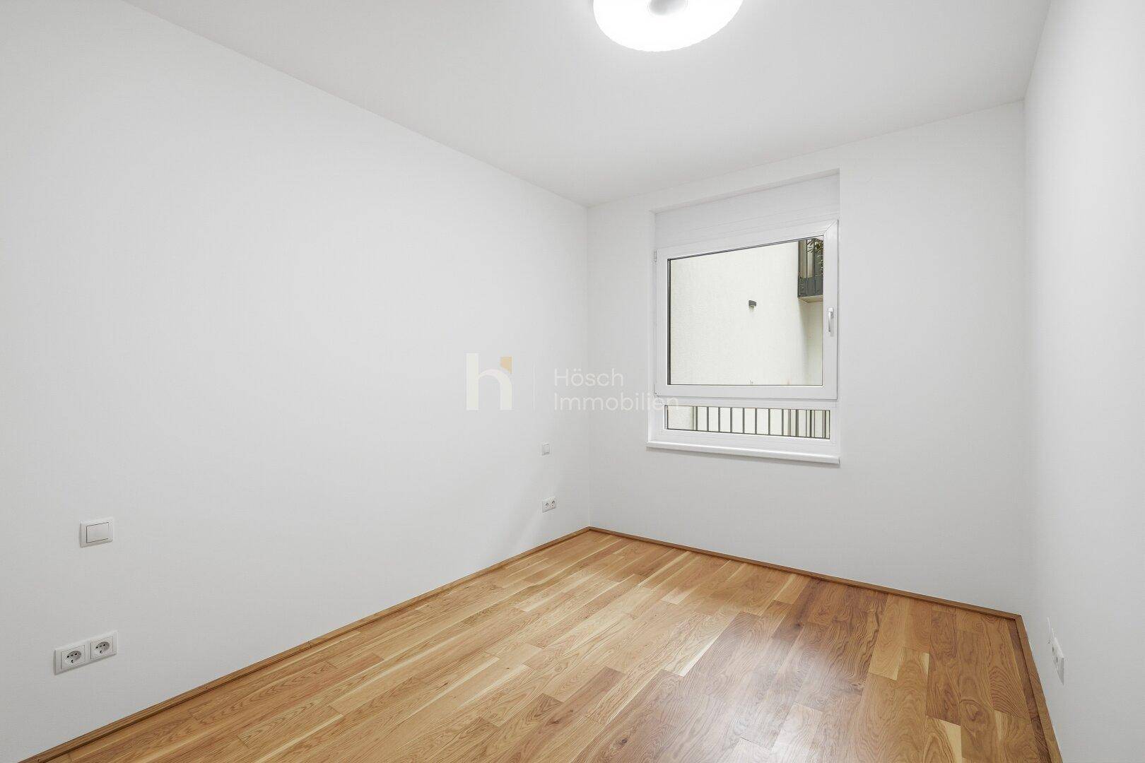 Helles Zimmer mit Holzboden und Fenster, das einen ruhigen Blick nach außen bietet.