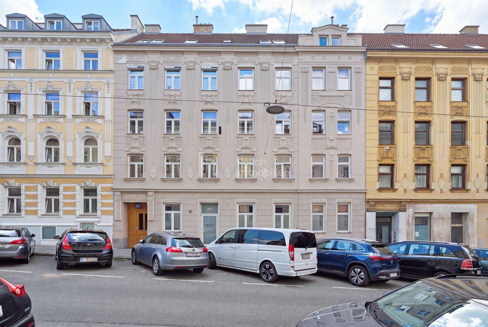 Historische Fassade eines Mehrfamilienhauses mit parkenden Autos auf der Straße.