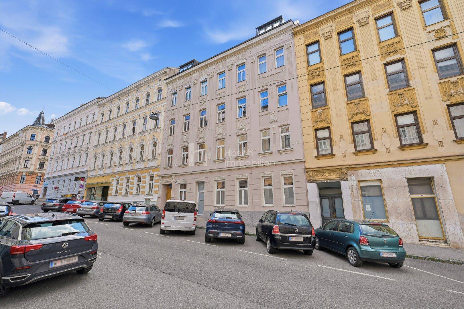 Historische Gebäudezeile mit geparkten Autos entlang einer belebten Stadtstraße.