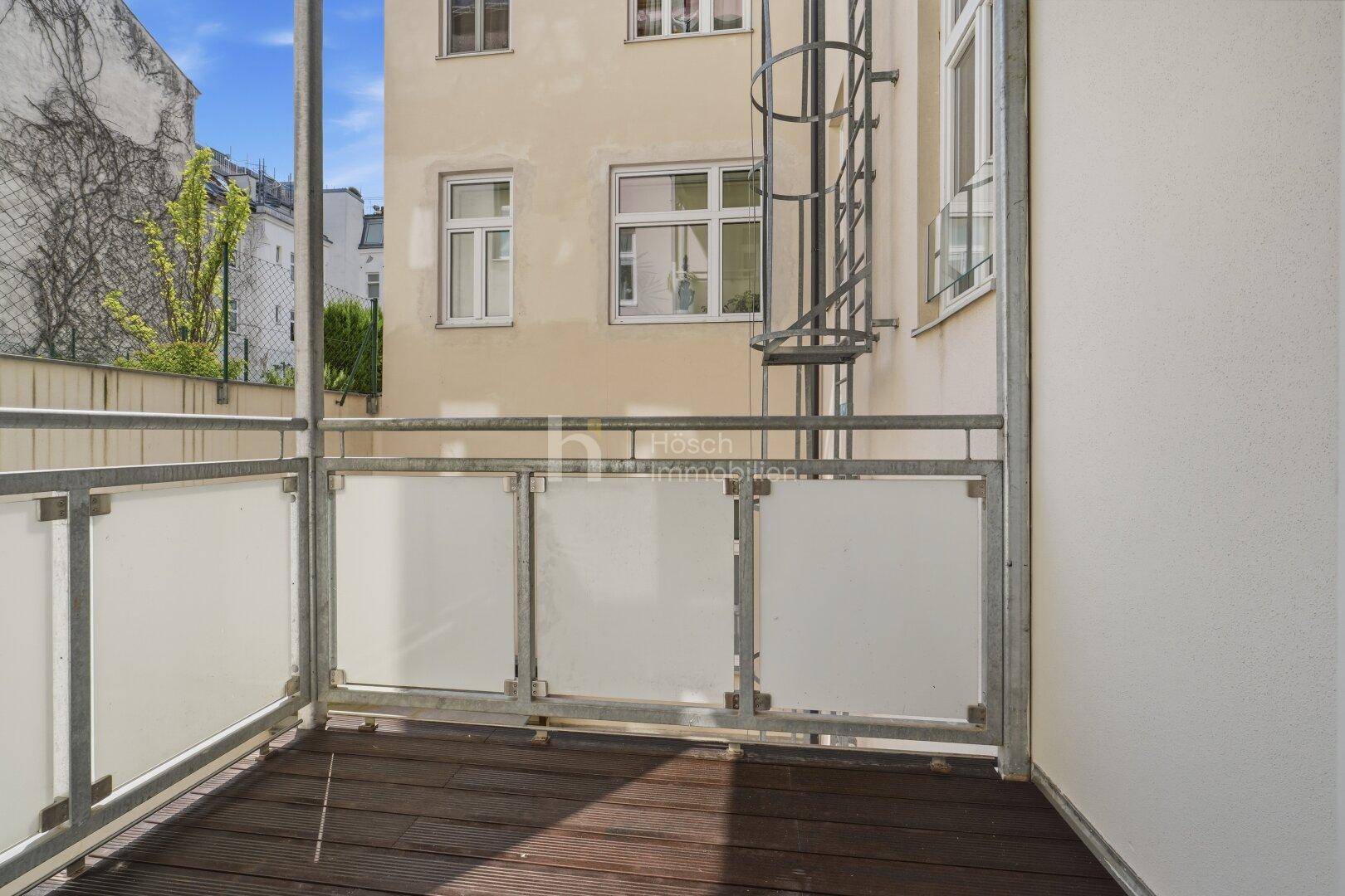 Kleiner Balkon mit Holzboden und Blick auf den Innenhof des Gebäudes.