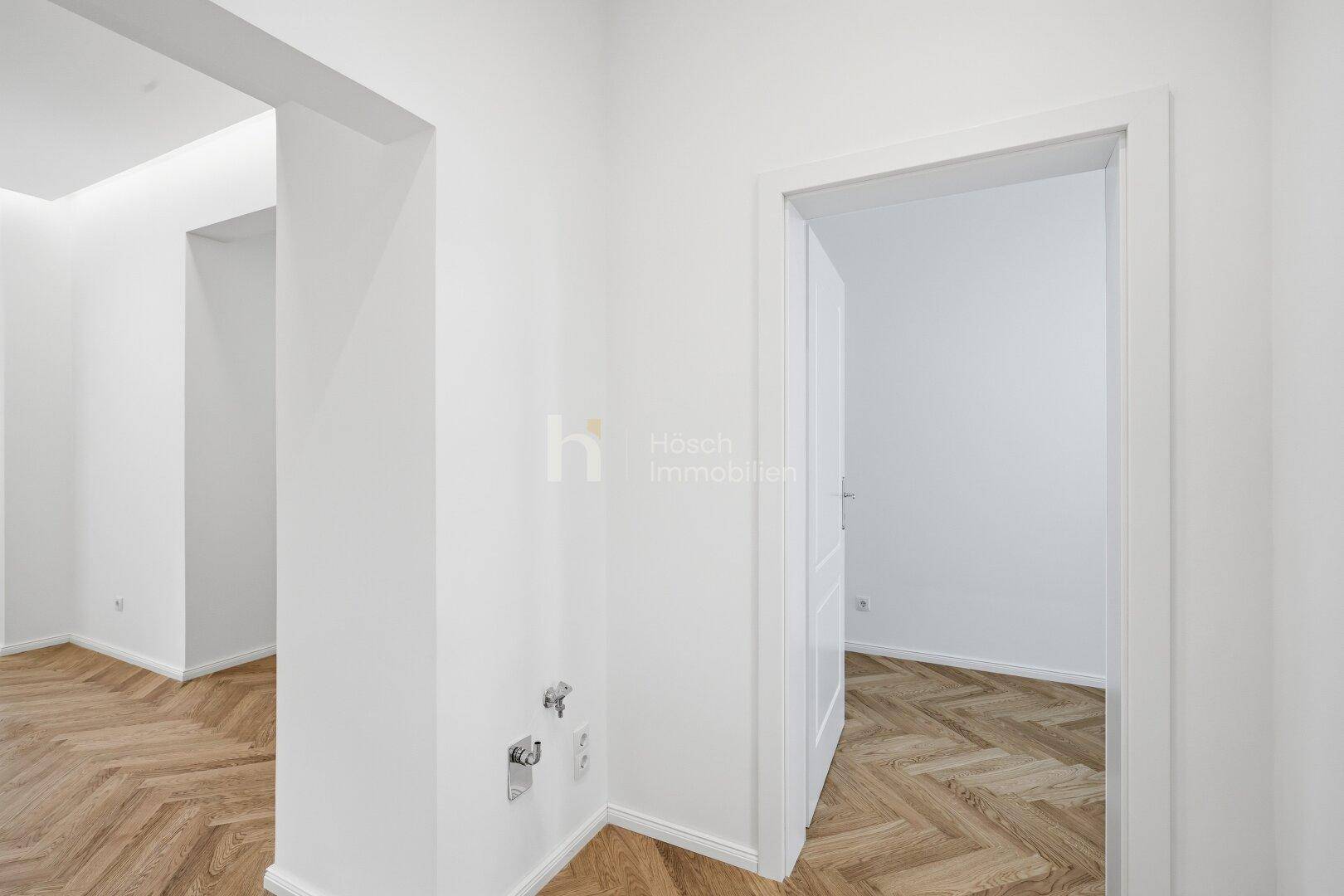 Heller Flur mit Fischgrätparkett und weiß gestrichenen Wänden, der zu einem weiteren Zimmer führt.