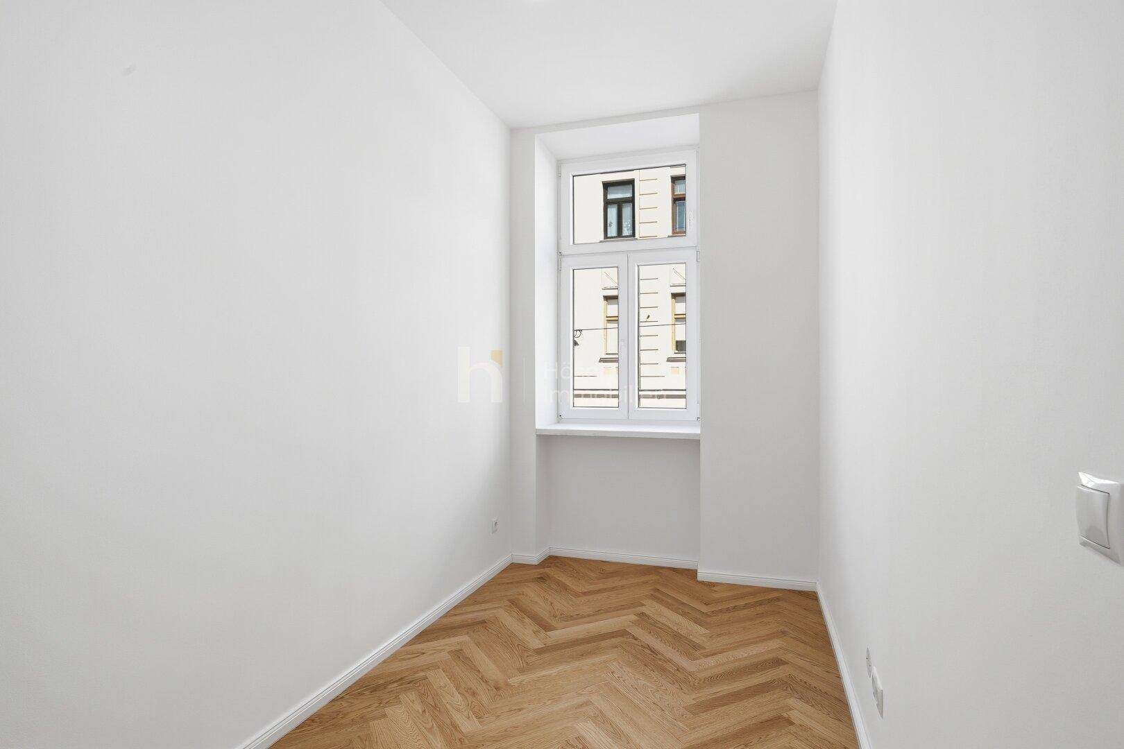 Kleines, helles Zimmer mit Fischgrätparkett und einem Fenster mit Blick auf die Stadt.