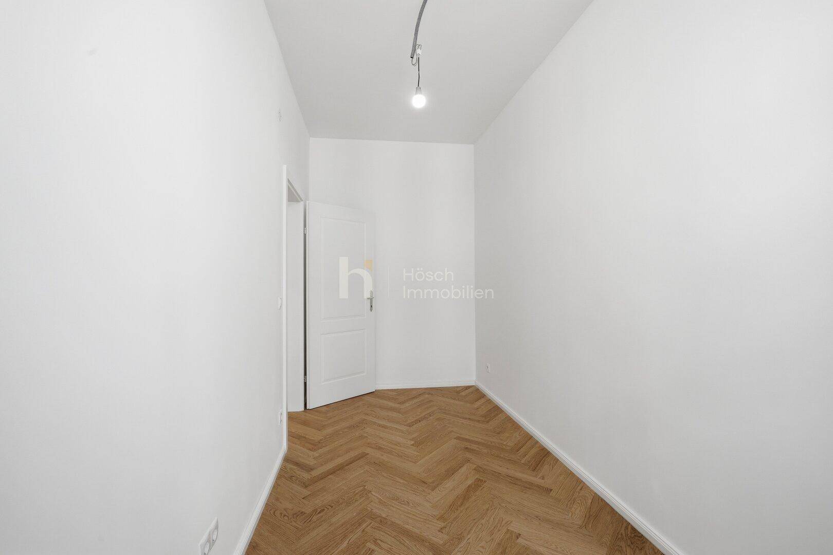 Heller Raum mit Fischgrätparkett und einer Tür, die zu einem weiteren Bereich führt.