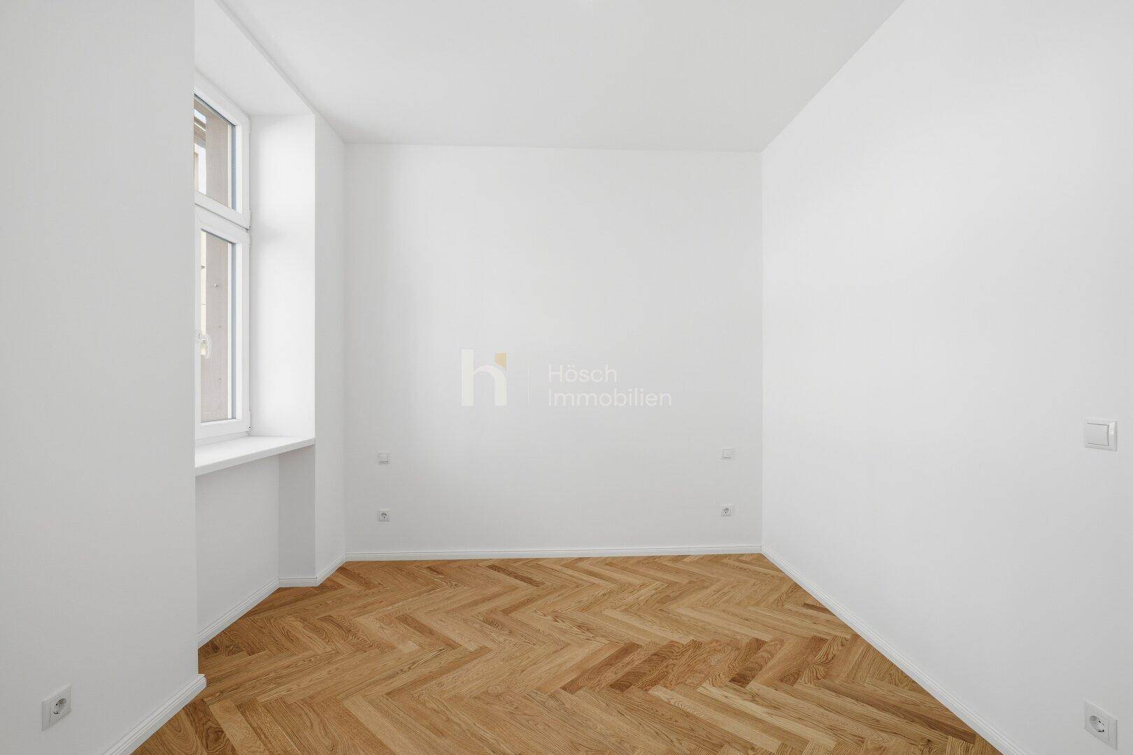 Ruhiges Zimmer mit Fischgrätparkett und einem großen Fenster, ideal als Schlaf- oder Arbeitszimmer.