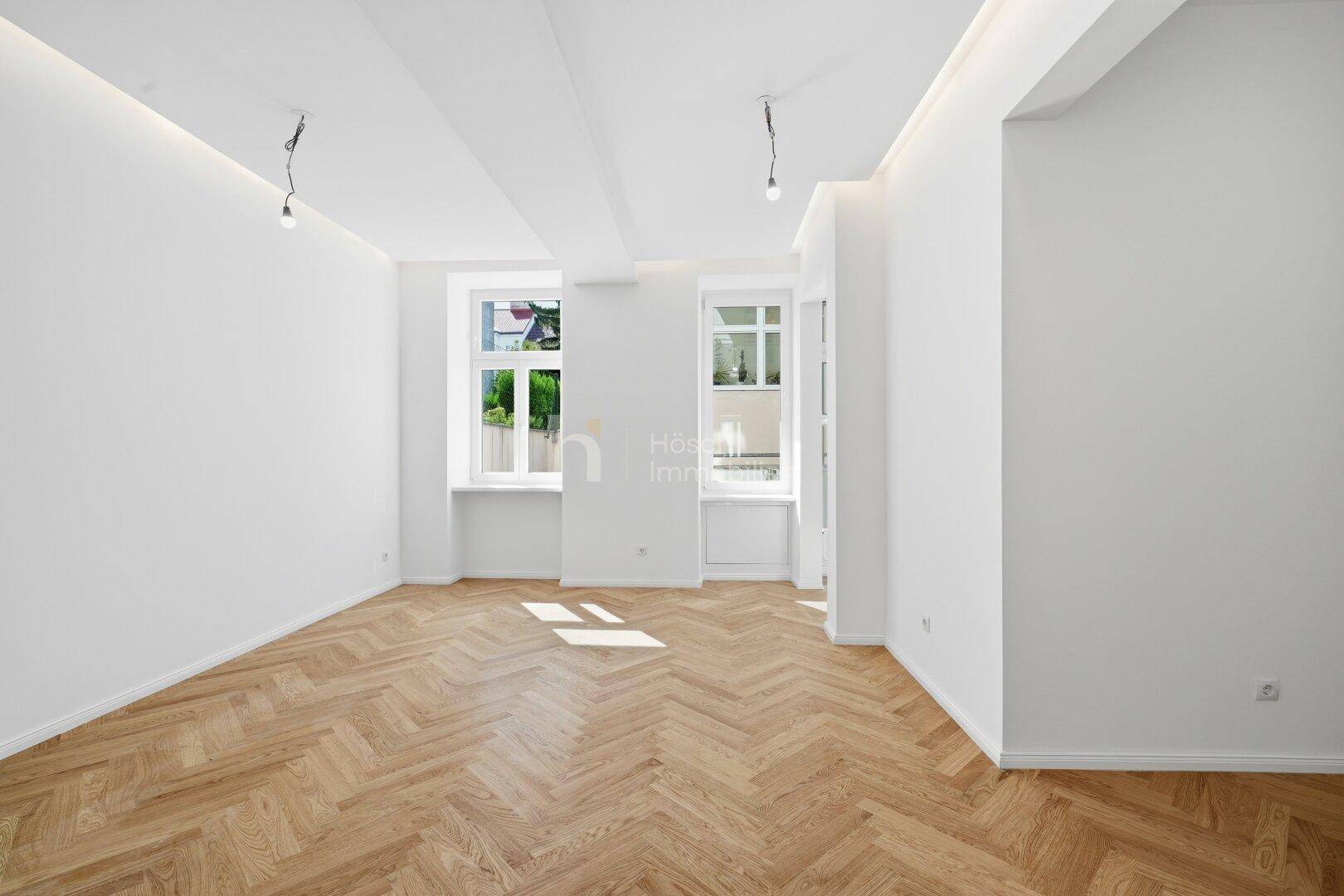 Geräumiges Zimmer mit elegantem Fischgrätparkett und viel Tageslicht durch die Fenster.