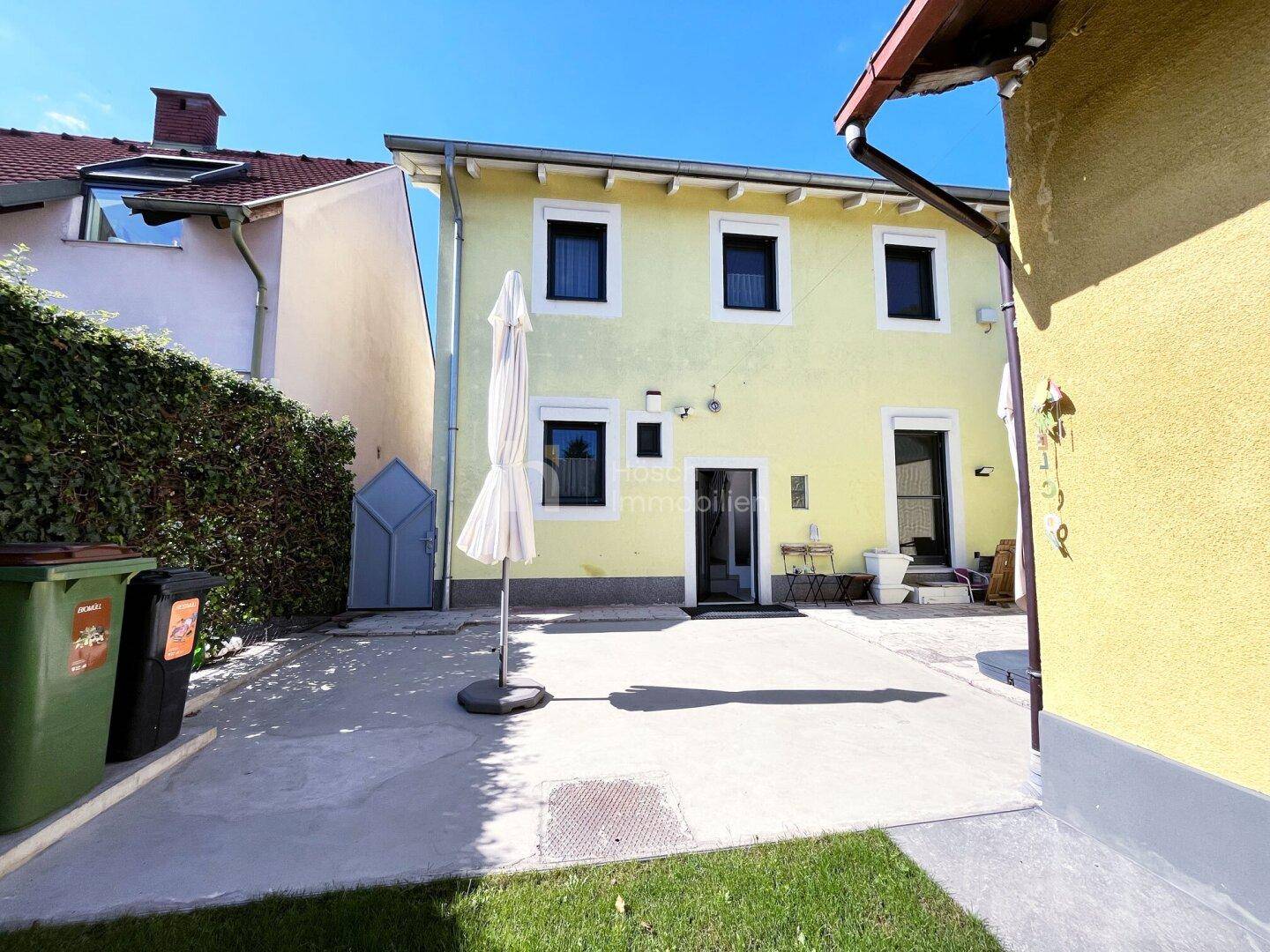 Hinterhof mit gepflasterter Terrasse, Sonnenschirm und Zugang zum Gartenbereich.