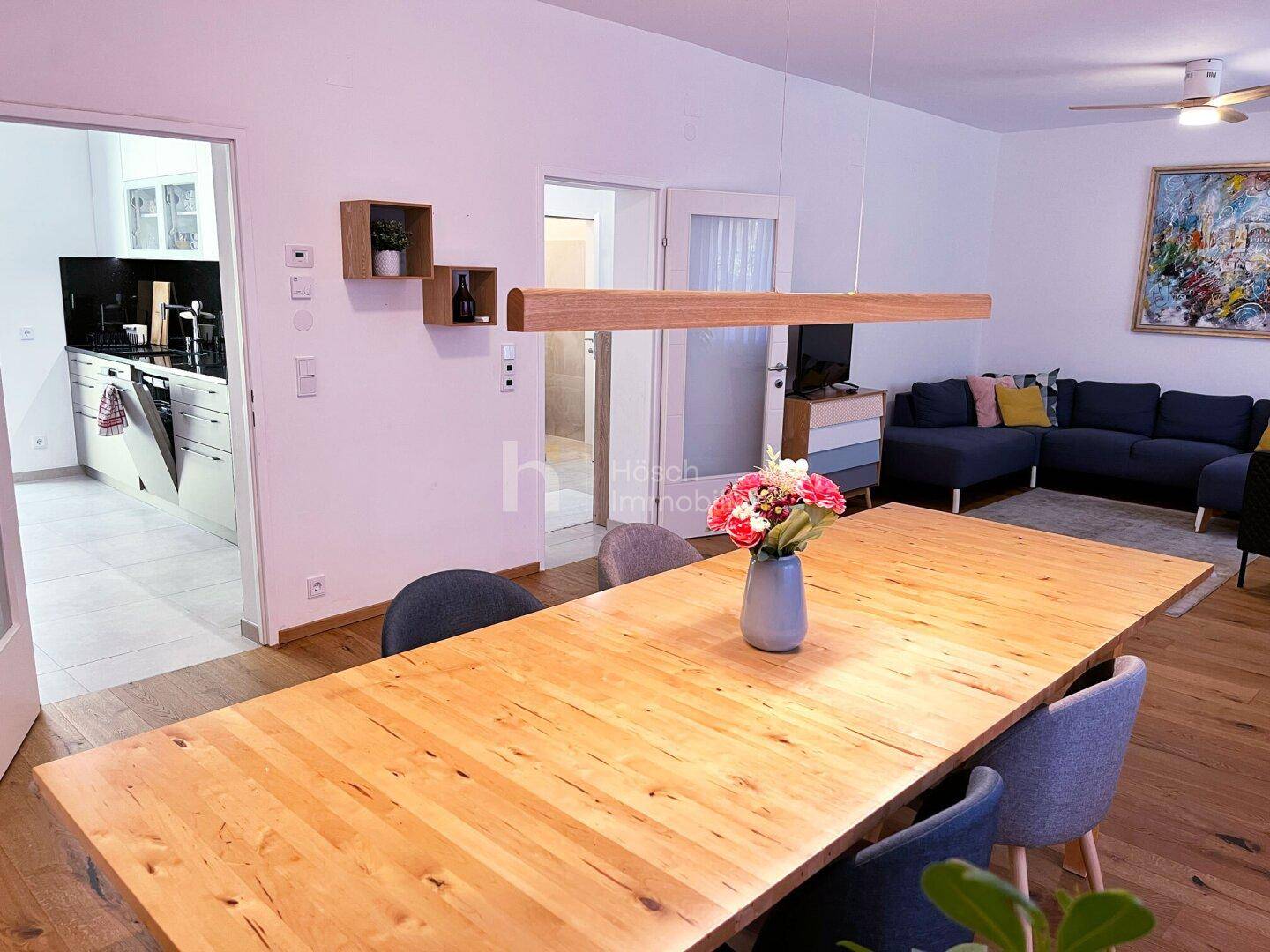 Heller Essbereich mit großem Holztisch, der zum offenen Wohnzimmer und zur Küche führt.