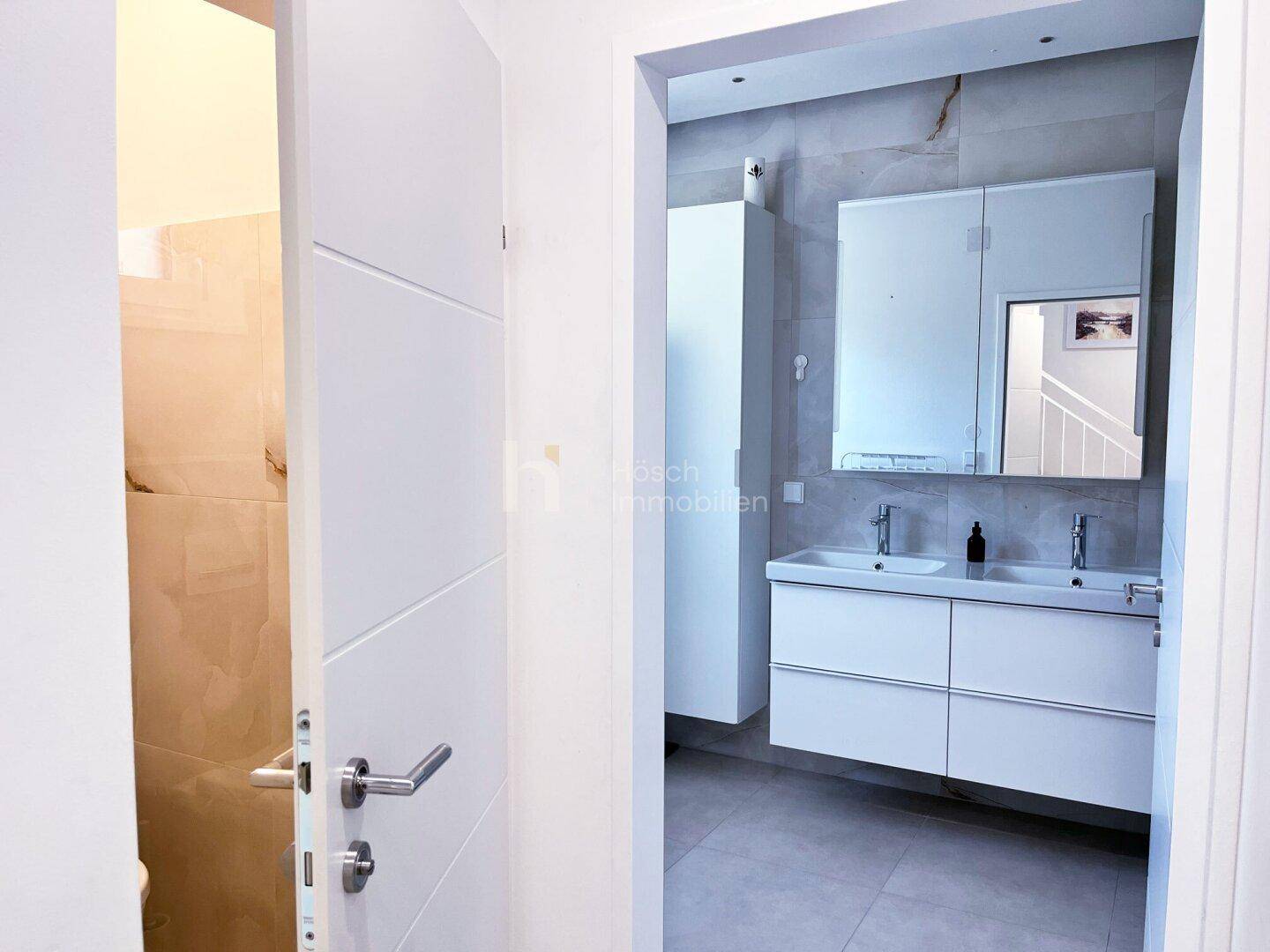 Modernes Badezimmer mit Doppelwaschbecken, großem Spiegelschrank und hellen Fliesen.
