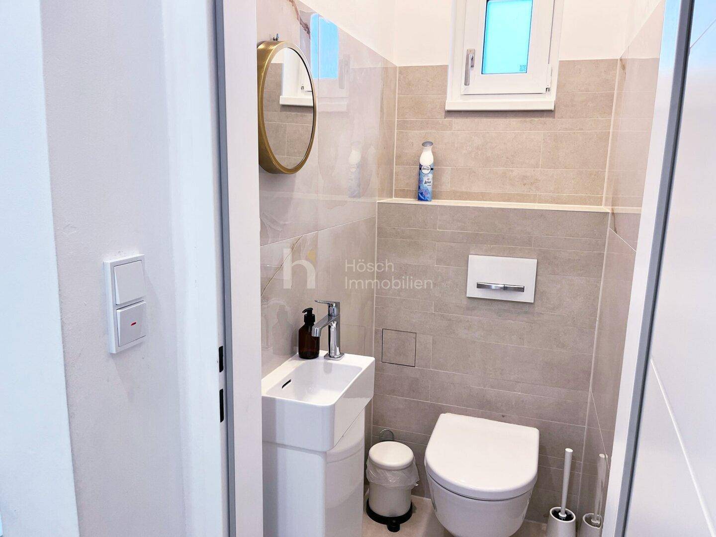 Modernes Gäste-WC mit wandhängender Toilette, kleinem Waschbecken und Fenster für Tageslicht.