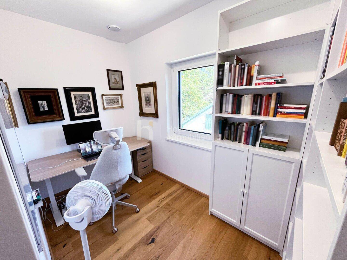Helles Heimbüro mit Schreibtisch, Bürostuhl, Bücherregal und Fenster für Tageslicht.