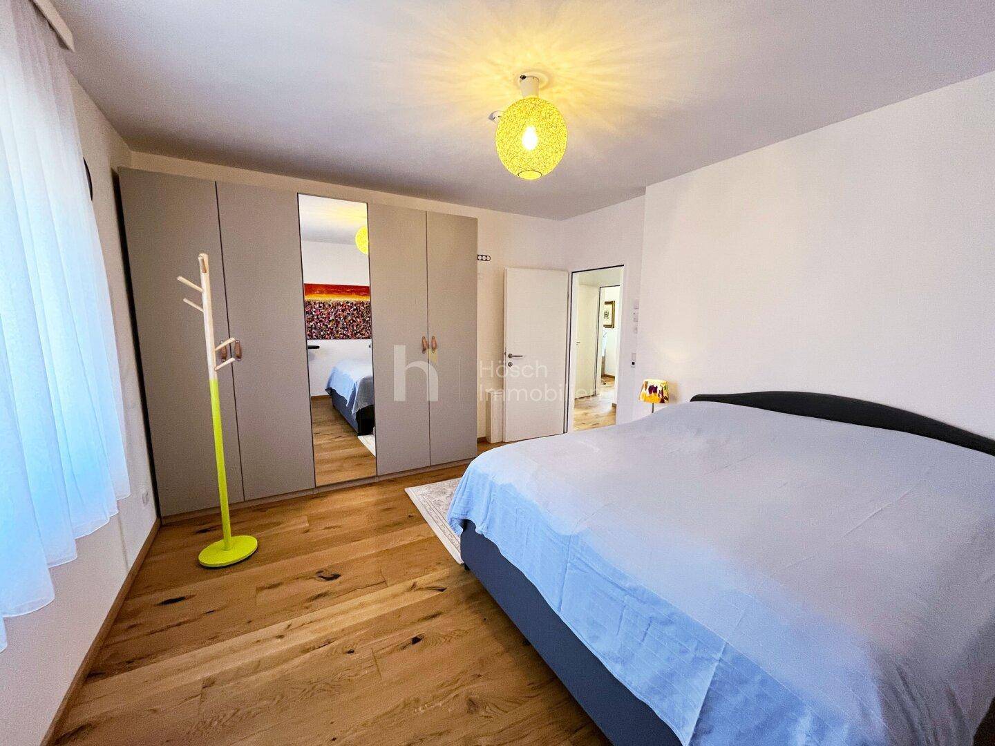 Geräumiges Schlafzimmer mit Doppelbett, großem Kleiderschrank mit Spiegeltüren und Holzboden.