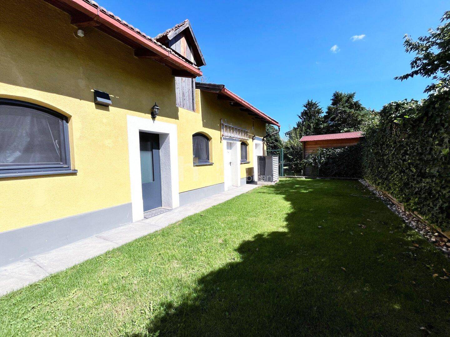Seitlicher Blick auf das gelbe Haus mit gepflegtem Rasen und grüner Hecke im Garten.