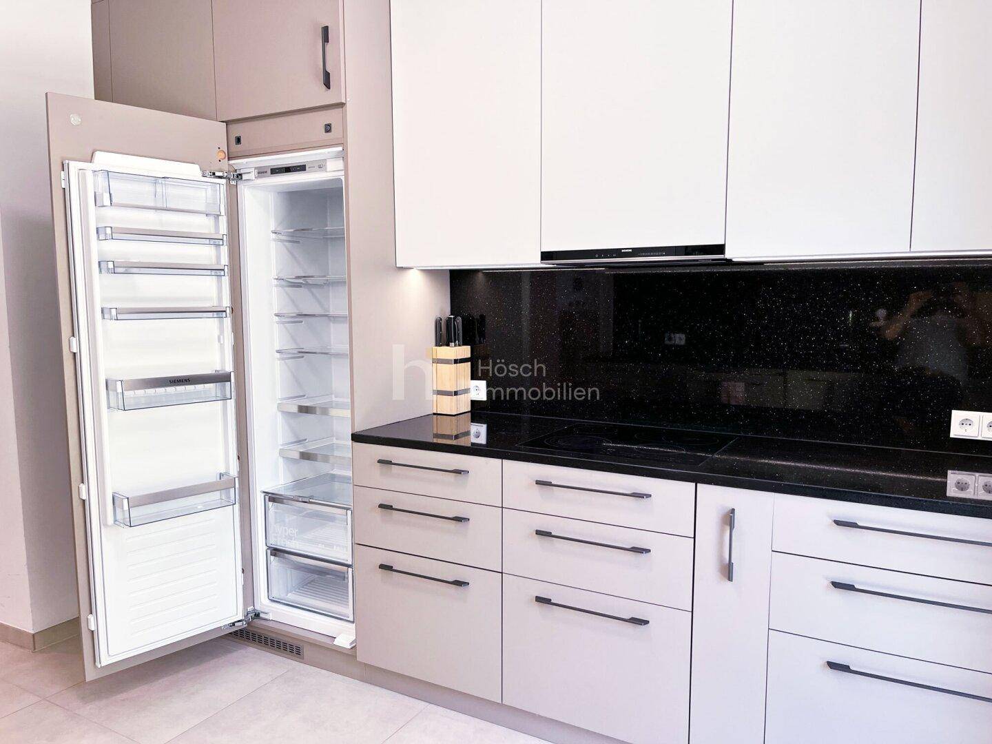 Moderne Küche mit integriertem Kühlschrank, schwarzen Arbeitsplatten und hellen Schränken.