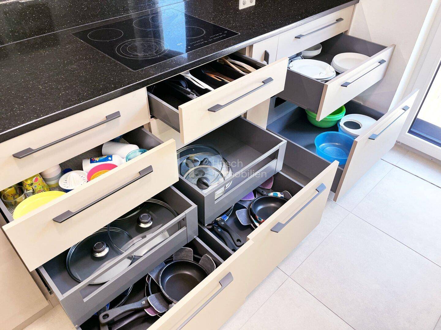 Gut organisierte Küchenschubladen mit Besteck, Geschirr und Kochutensilien für effizientes Kochen.