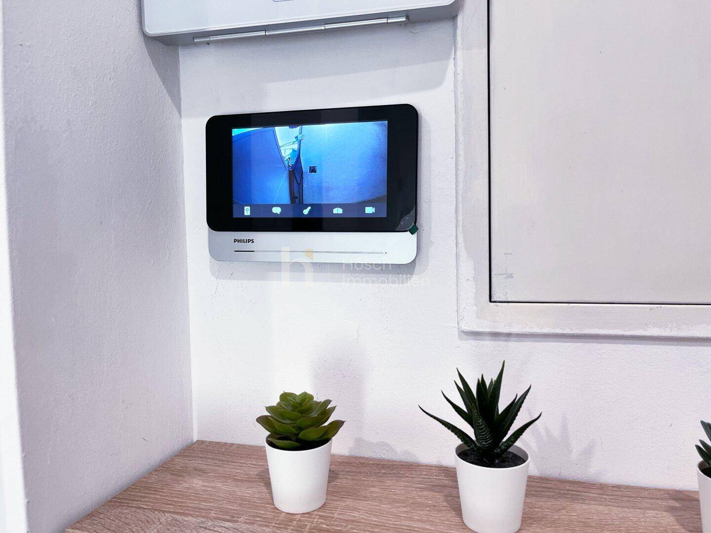 Modernes Video-Gegensprechanlage-System an der Wand, dekoriert mit kleinen Pflanzen.