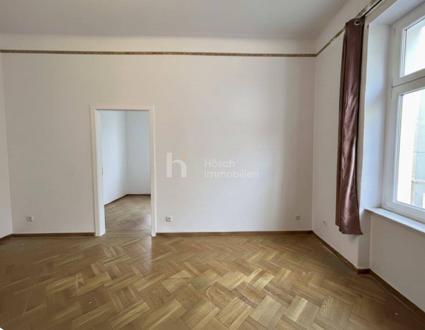 Heller Raum mit Fischgrätparkett und einem großen Fenster, ideal für Wohn- oder Schlafzimmer.