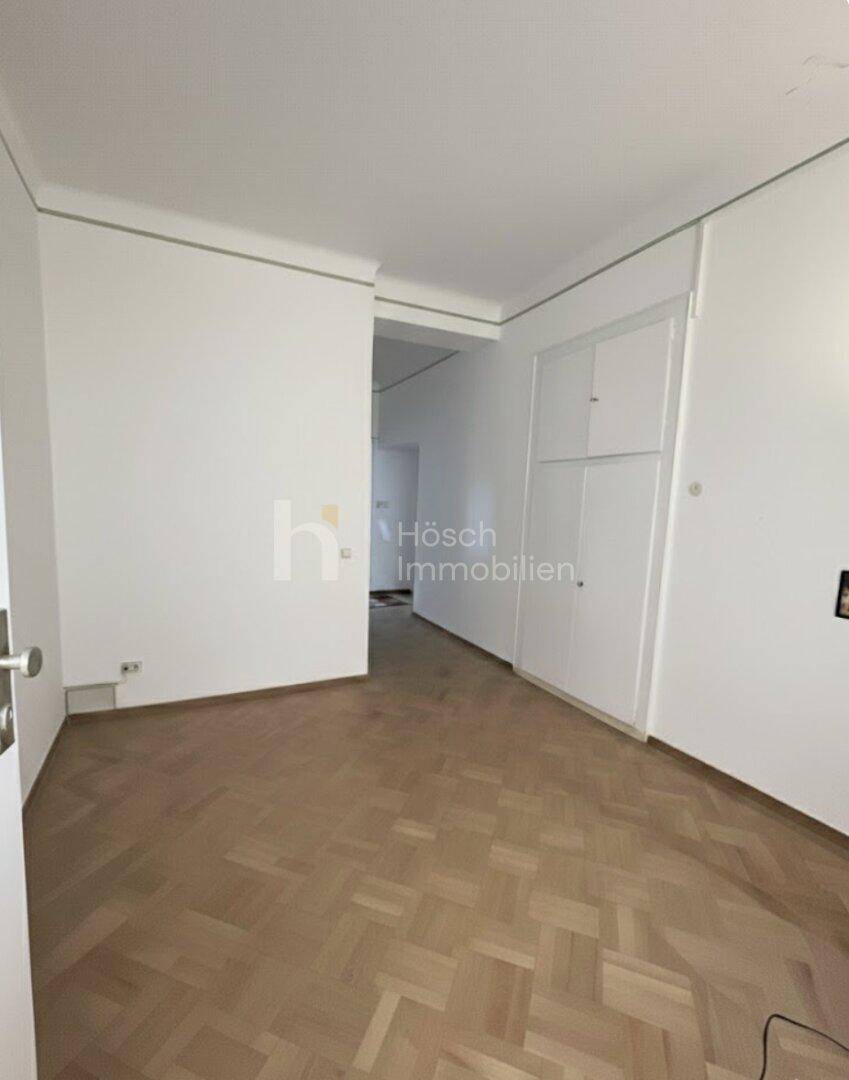 Leeres Zimmer mit Fischgrätparkett und einem integrierten Wandschrank.