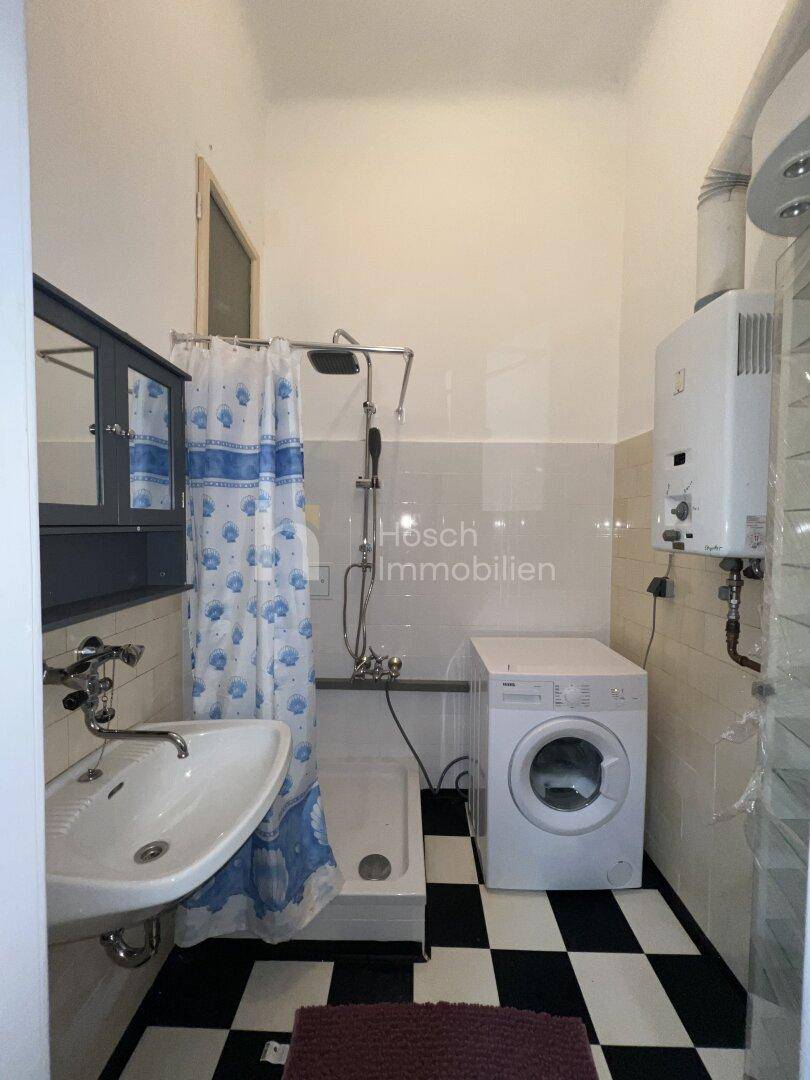 Kleines Badezimmer mit Dusche, Waschbecken, Waschmaschine und schwarz-weißem Fliesenboden.