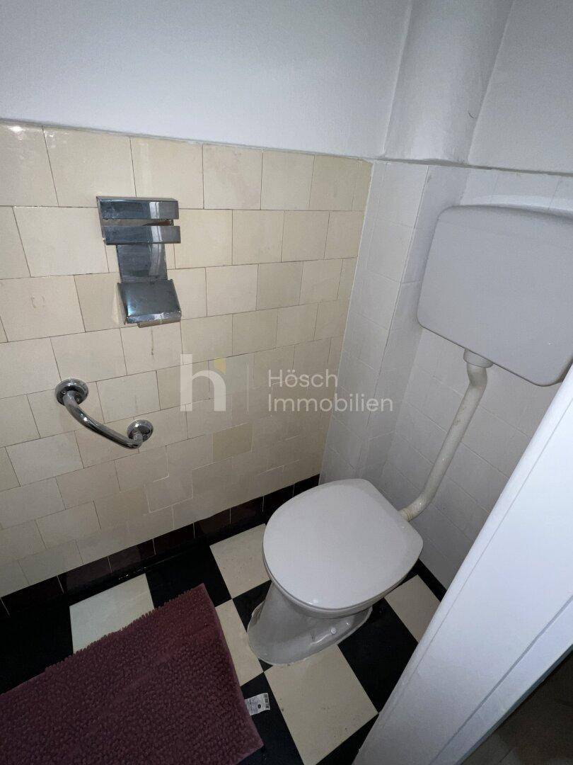 Separate Toilette mit Haltegriffen und markantem schwarz-weißem Fliesenboden.