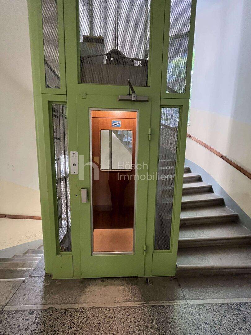 Historischer Aufzug in einem Treppenhaus, der den Zugang zu den oberen Etagen ermöglicht.