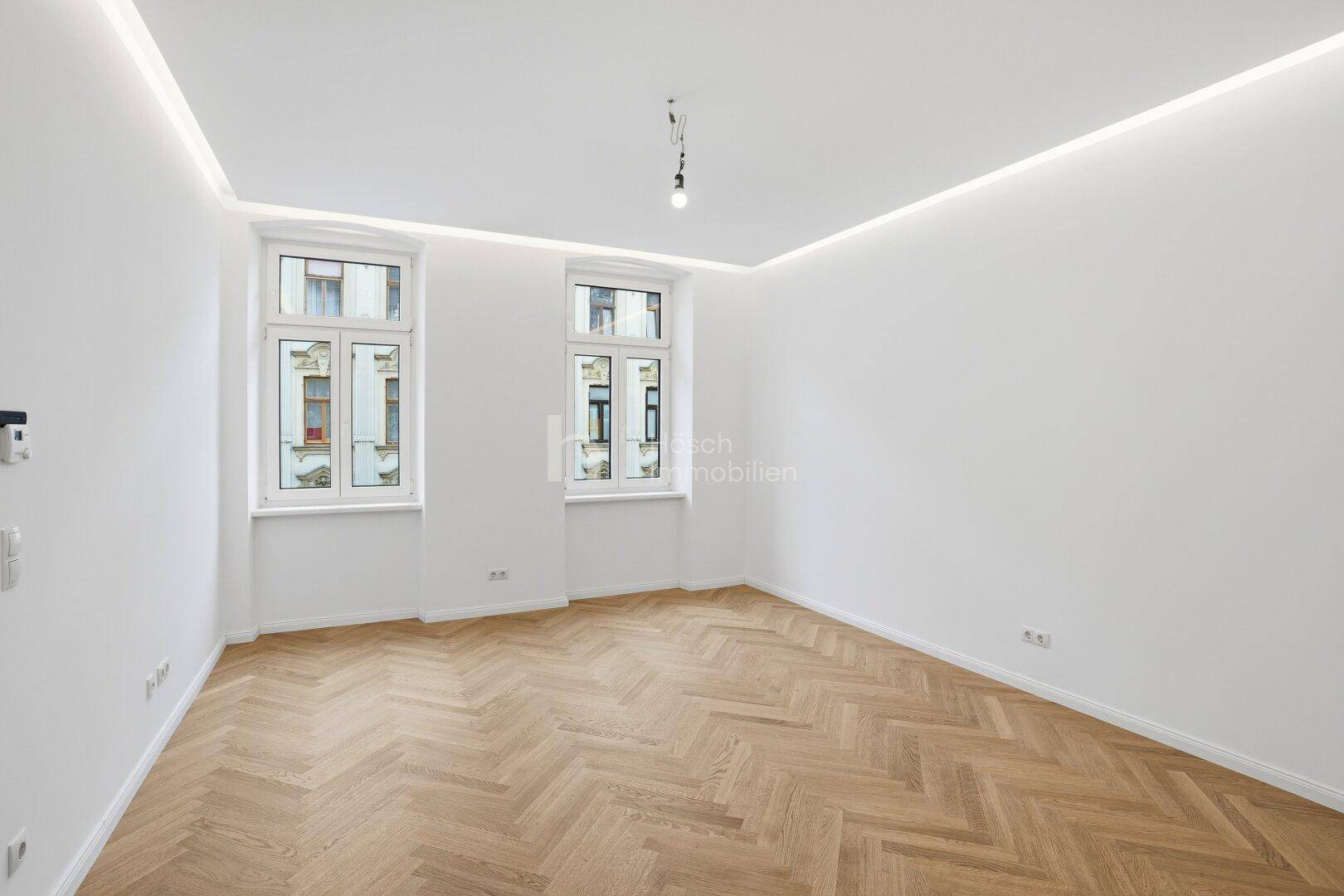 Geräumiger, heller Raum mit Fischgrätparkett und hohen Decken, ideal für Wohnzwecke.