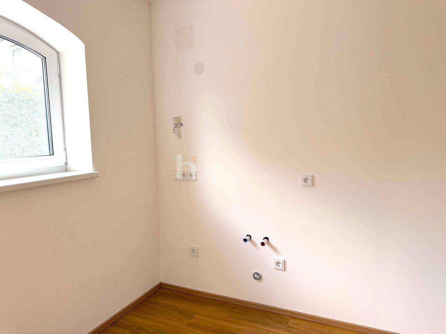 Wand mit Anschlüssen für Wasser und Elektrizität in einem hellen Raum mit Bogenfenster.