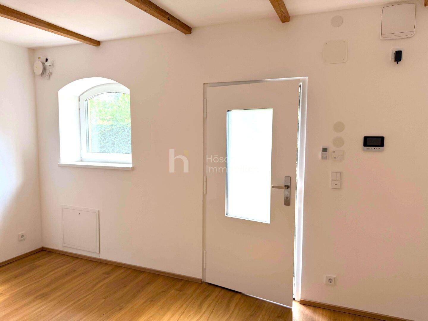 Eingangsbereich mit einer modernen Tür und einem Bogenfenster, ergänzt durch Holzbalken.