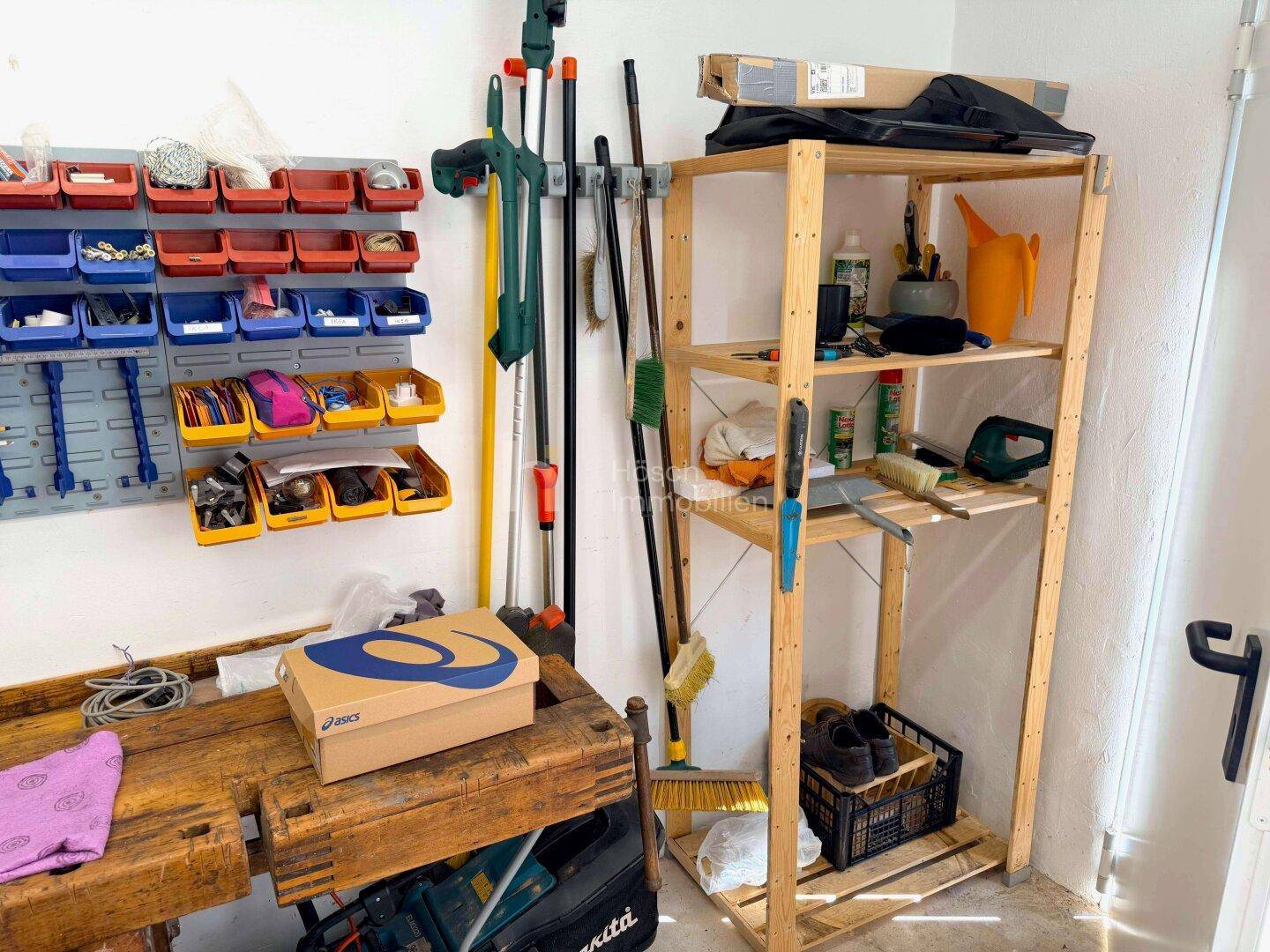 Lagerbereich mit Holzregalen und Werkzeugaufbewahrung an der Wand in einem hellen Raum.