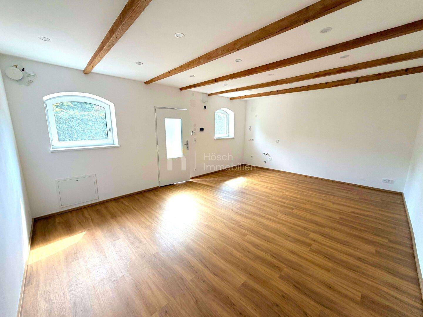 Heller, geräumiger Wohnbereich mit sichtbaren Holzbalken und Laminatboden, viel Tageslicht.