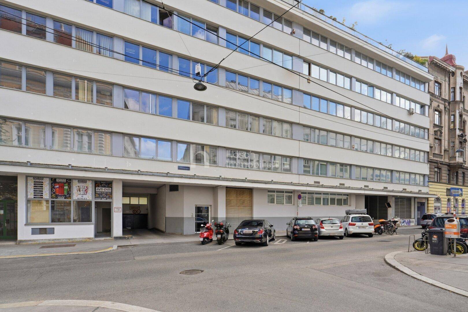 Nahaufnahme der modernen Gebäudefassade mit vielen Fenstern und parkenden Fahrzeugen davor in der Stadt.