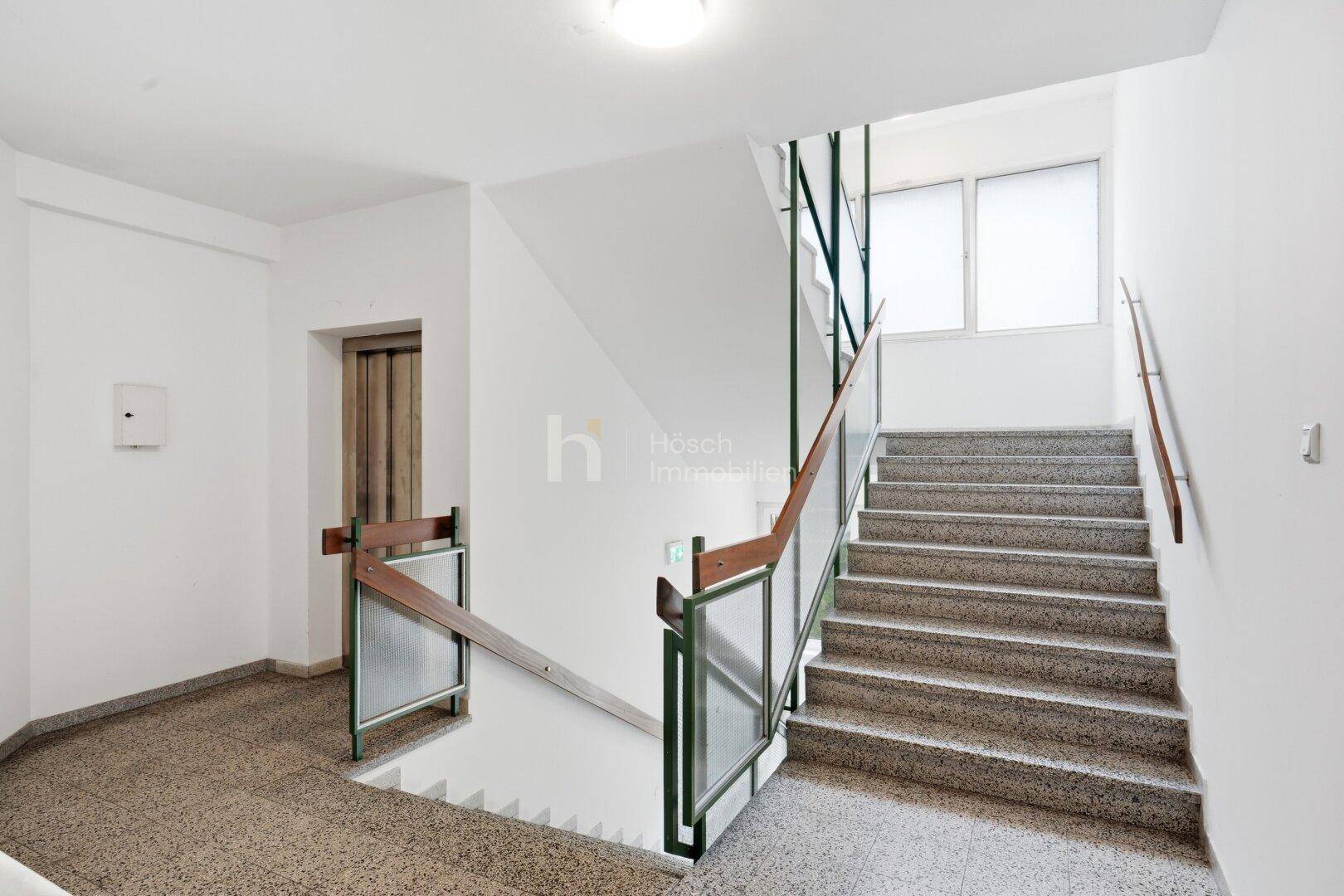 Helles Treppenhaus mit Terrazzoboden und Geländer in einem Mehrfamilienhaus mit natürlichem Licht.