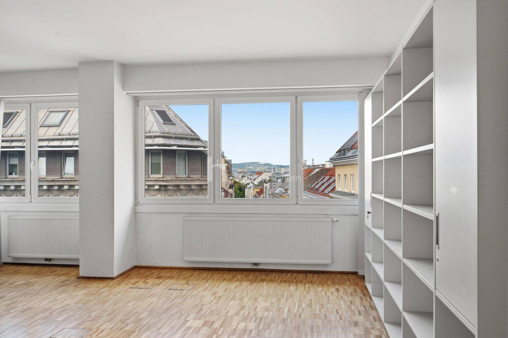 Heller Büroraum mit Parkettboden, Einbauregalen und weitem Blick über die Stadt.