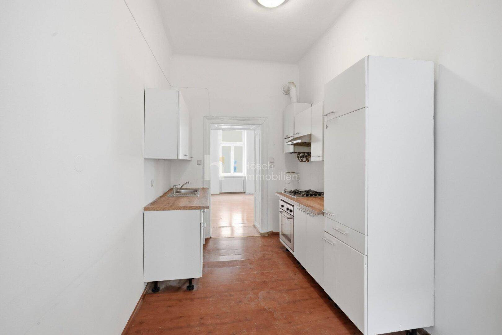 Schmale Küche mit weißen Schränken, Holz-Arbeitsplatte und Gasherd, bietet Zugang zu einem weiteren Raum.