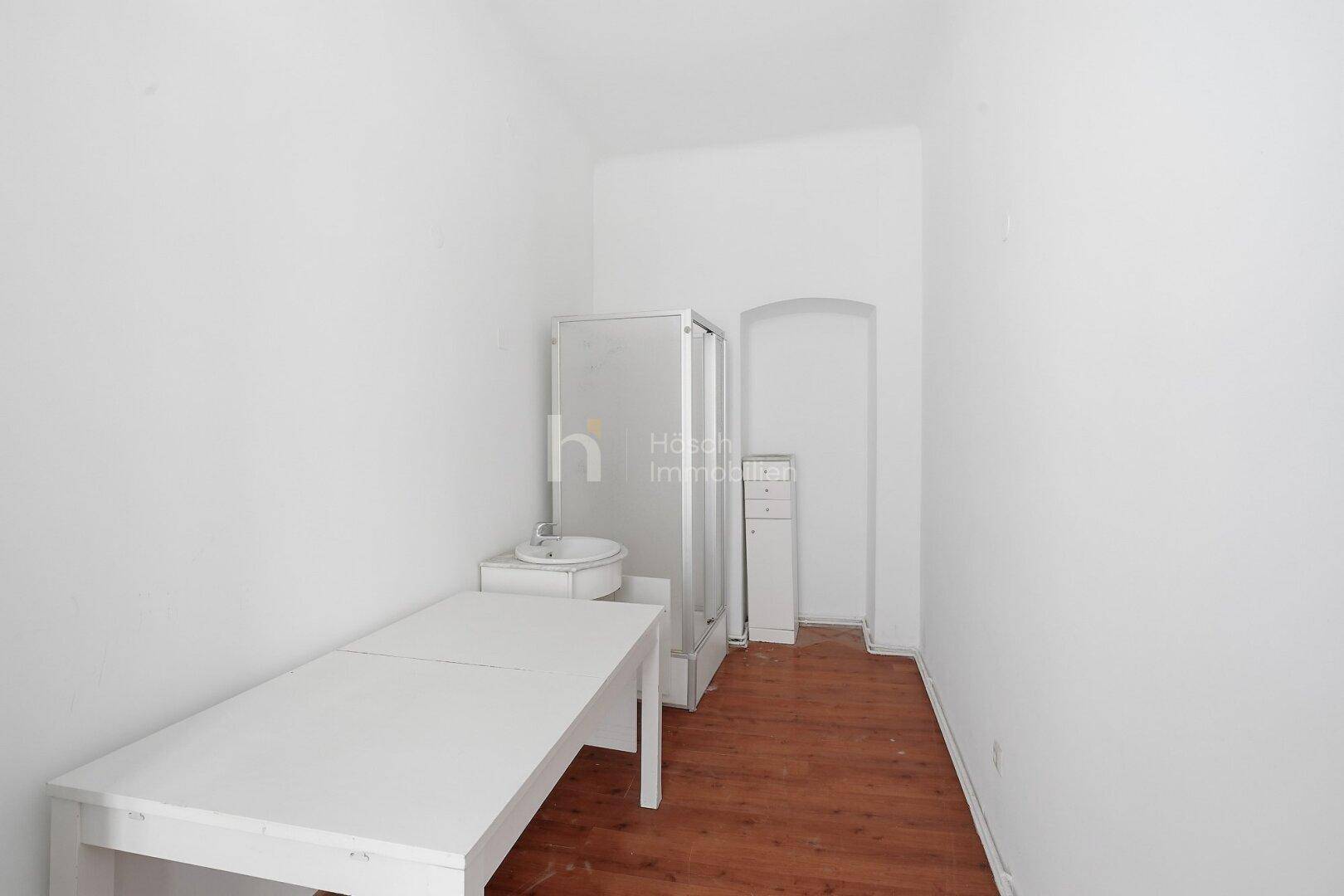 Kleiner Raum mit Duschkabine, Waschbecken und Holzboden, nutzbar als einfaches Badezimmer oder Abstellraum.