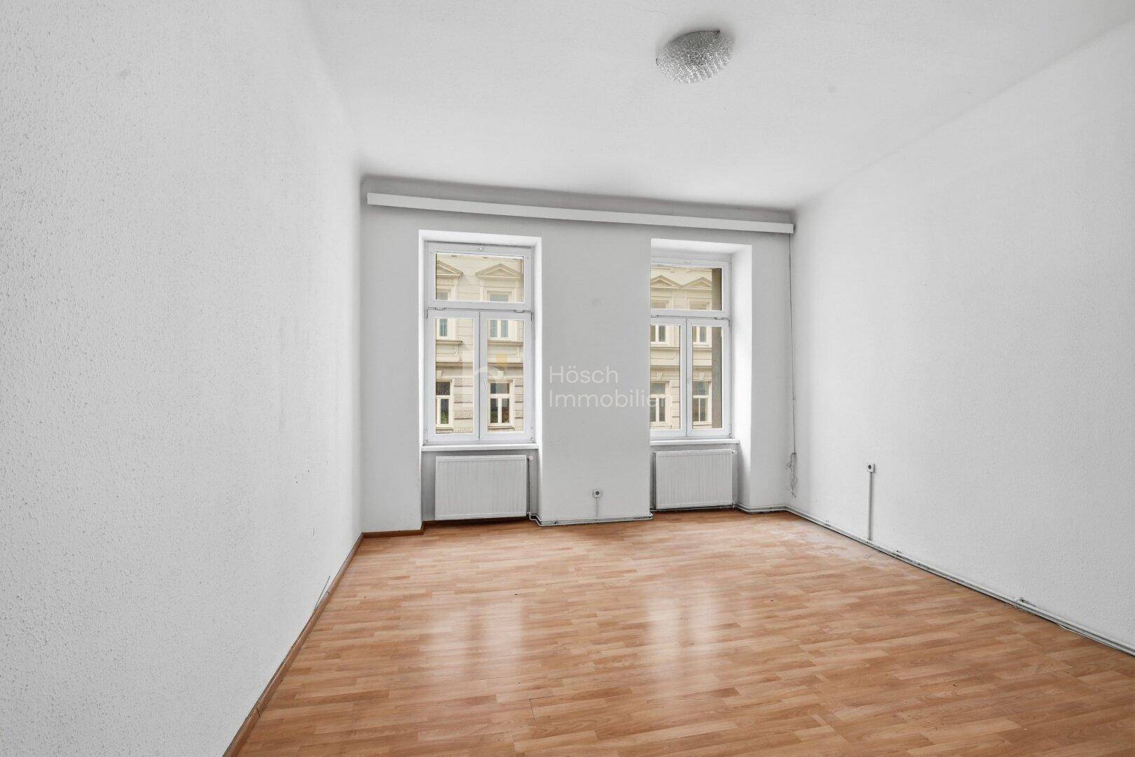 Geräumiges Zimmer mit zwei Fenstern, Laminatboden und weißen Wänden, bereit zur individuellen Gestaltung.