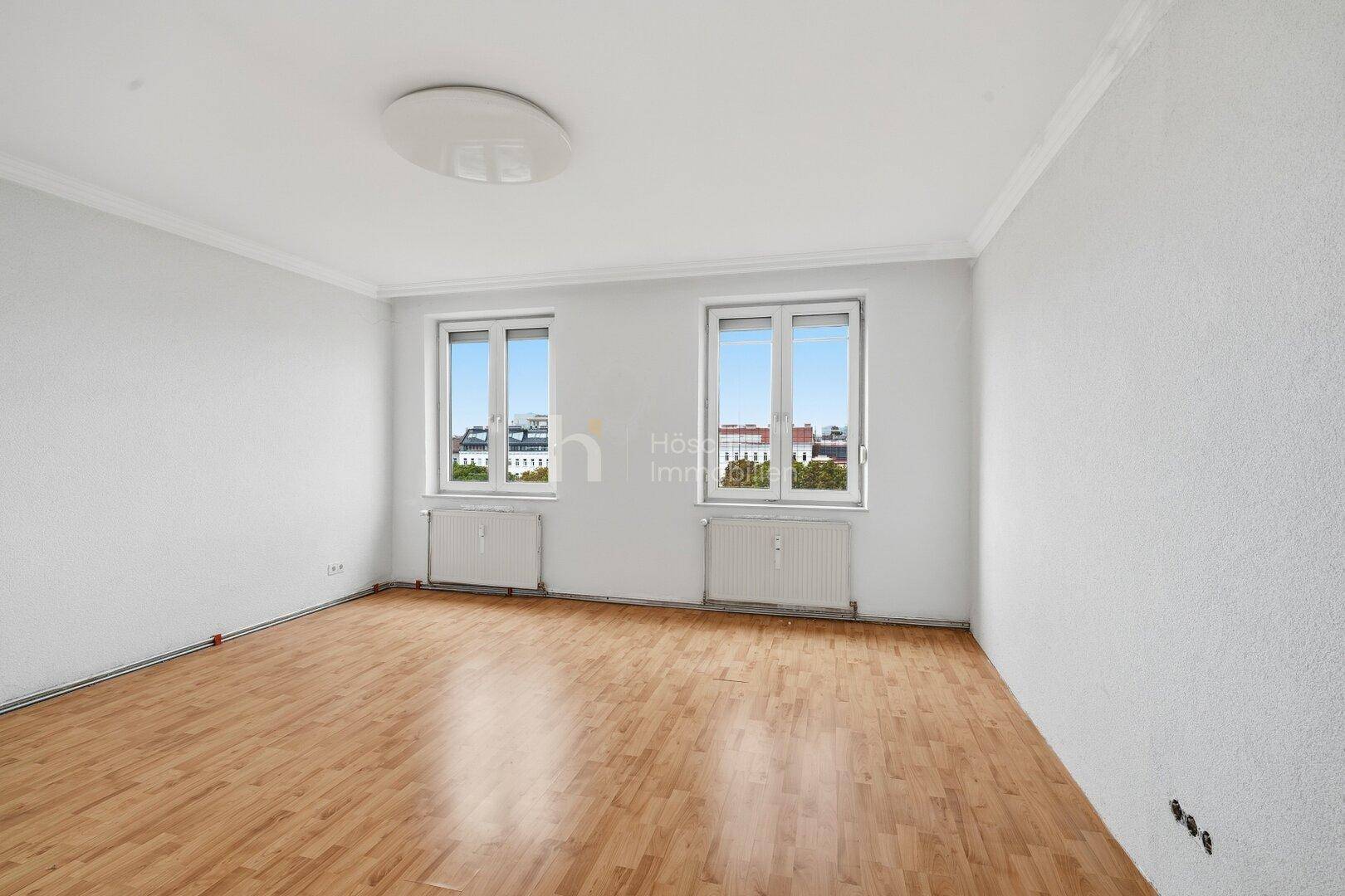 Geräumiges Zimmer mit hellem Parkettboden und zwei Fenstern für viel Tageslicht.