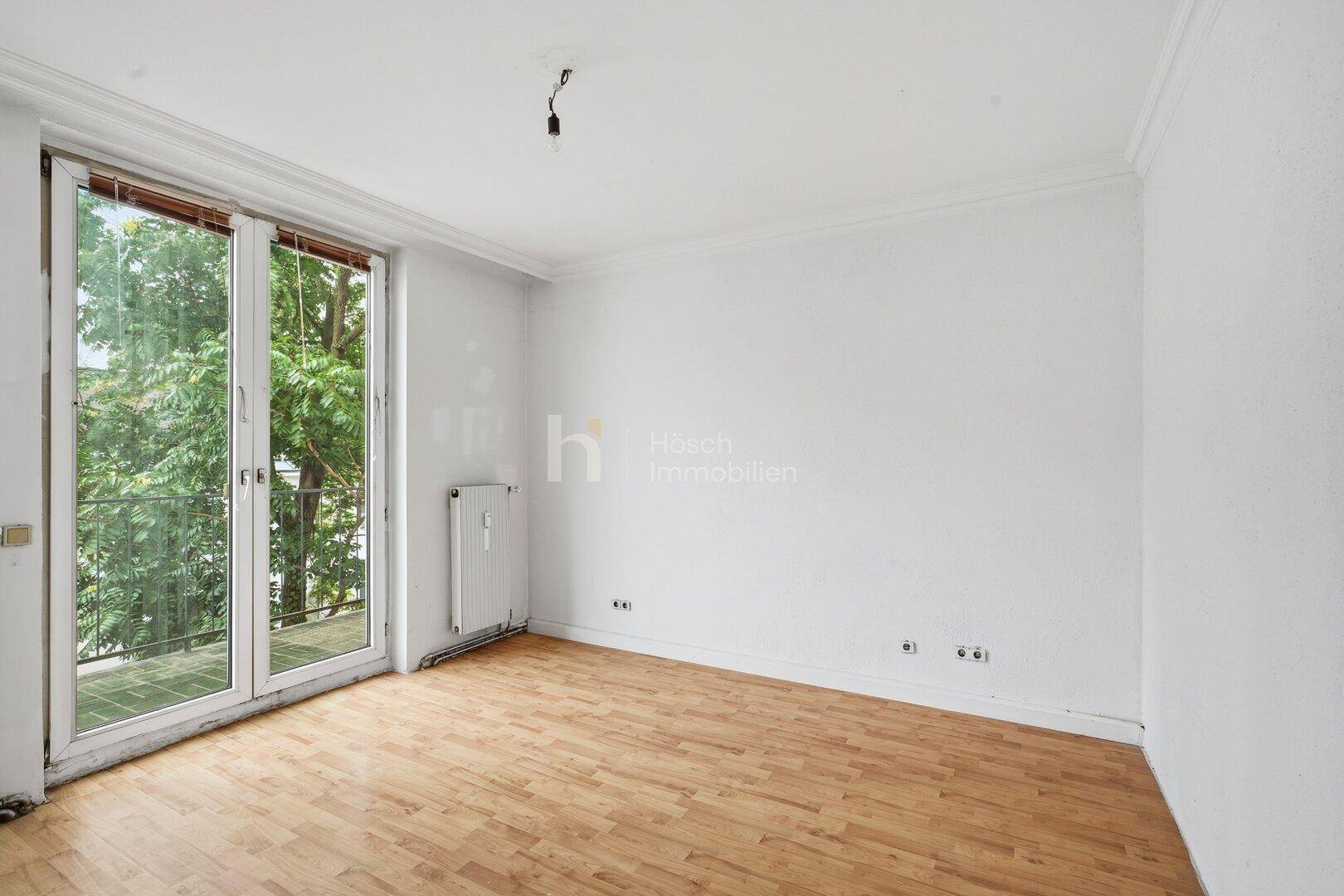 Heller Raum mit Holzboden und großer Glastür, die Zugang zu einem Außenbereich bietet.